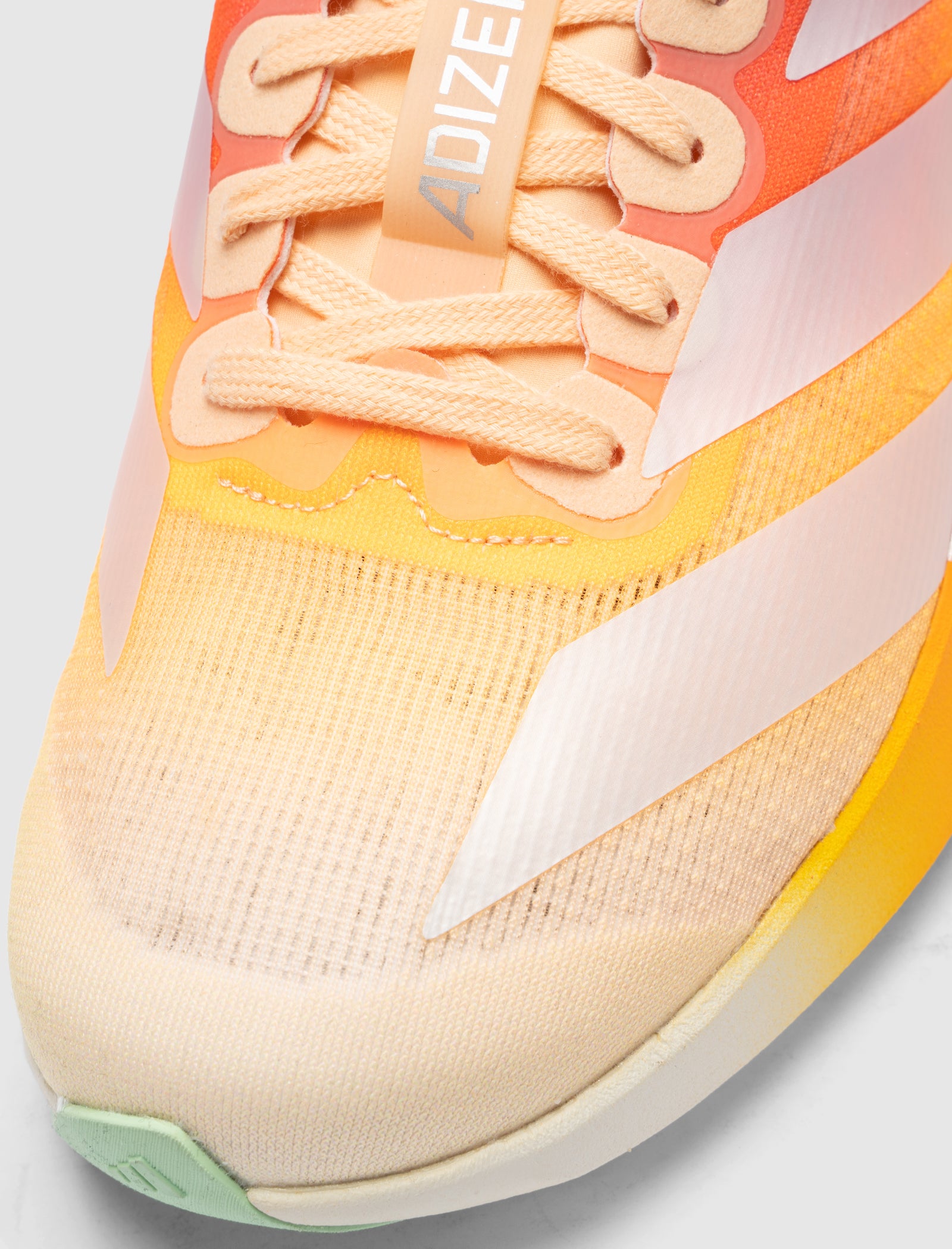 Close-up of the DO NOT DUPLICATE EVO SL DAYGLOW "ORANGE/WHITE" running shoes, showcasing orange, yellow, and beige mesh with white stripes, light peach laces, a gradient design, and "ADIZERO" on the tongue.