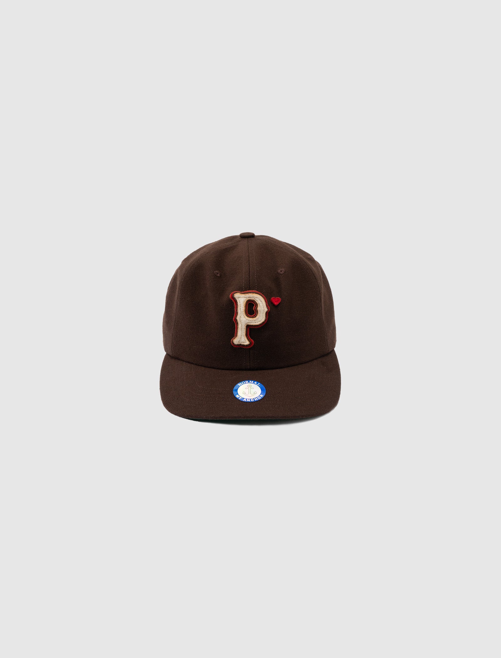 The WOOL BASEBALL "P" HAT is a brown wool snapback cap with a beige and red letter P on the front, shown against a light gray background. It features an adjustable fit and a round blue and white sticker on the brim.