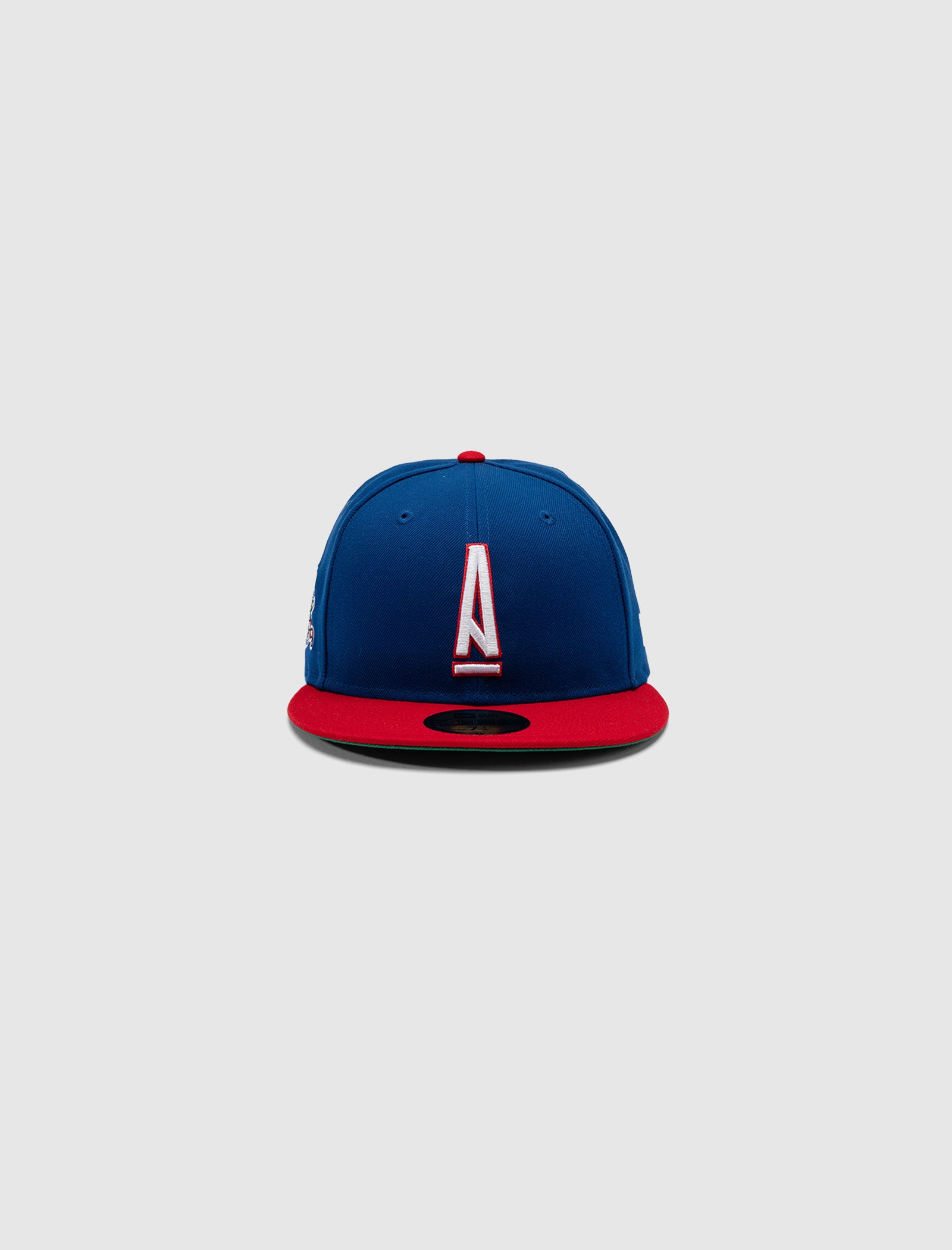 The A MA MANIÉRE 5950 A LOGO HAT by New Era features a blue crown, red brim, and a bold white and red "A" on the front, centered against a plain gray background.