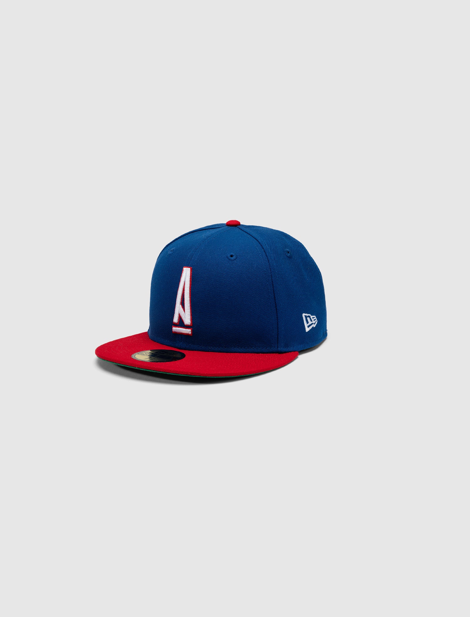 The A MA MANIÉRE 5950 A LOGO HAT by New Era features a blue crown, red brim, and a white and red letter A on the front, shown against a plain gray background.