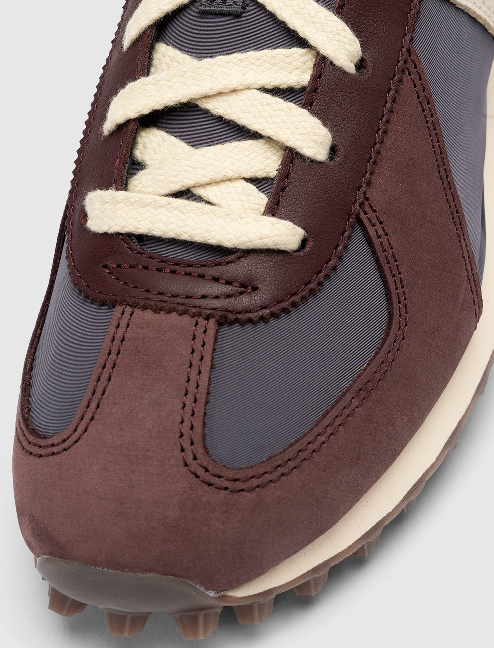 Close-up of the DND BW RUN HARLEM'S BEST sneakers, featuring cream laces, dark maroon suede overlays, dark gray fabric panels, an off-white sole, and a brown textured rubber outsole for a stylish finish.