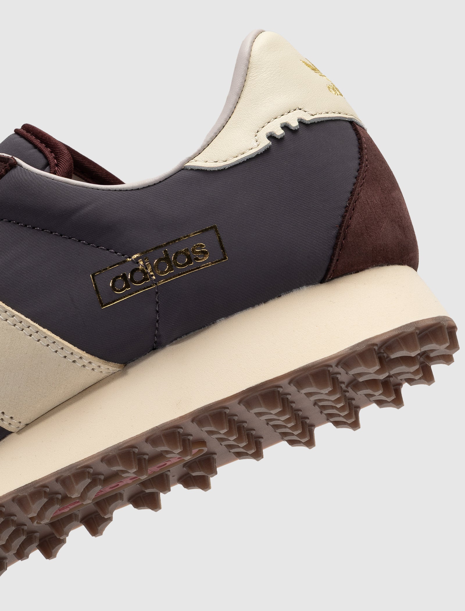 Close-up of the heel and side of the DND BW RUN HARLEM'S BEST, a low top sneaker in gray, cream, and brown with a gold Adidas logo and textured brown outsole.