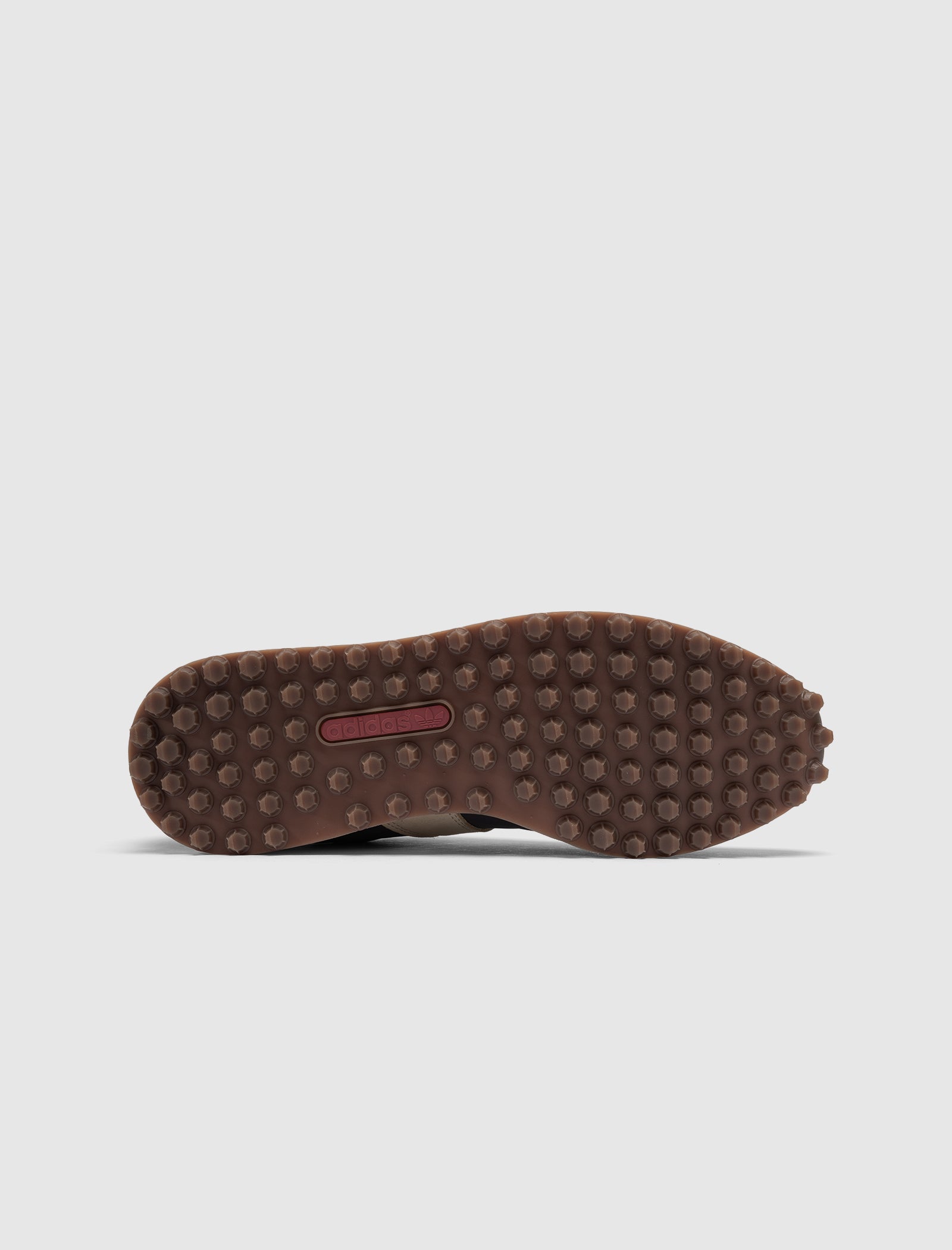 The DND BW RUN HARLEM'S BEST low top sneaker features a brown rubber sole with numerous round studs for traction and a small red rectangular accent at the midfoot, as seen from the bottom view.