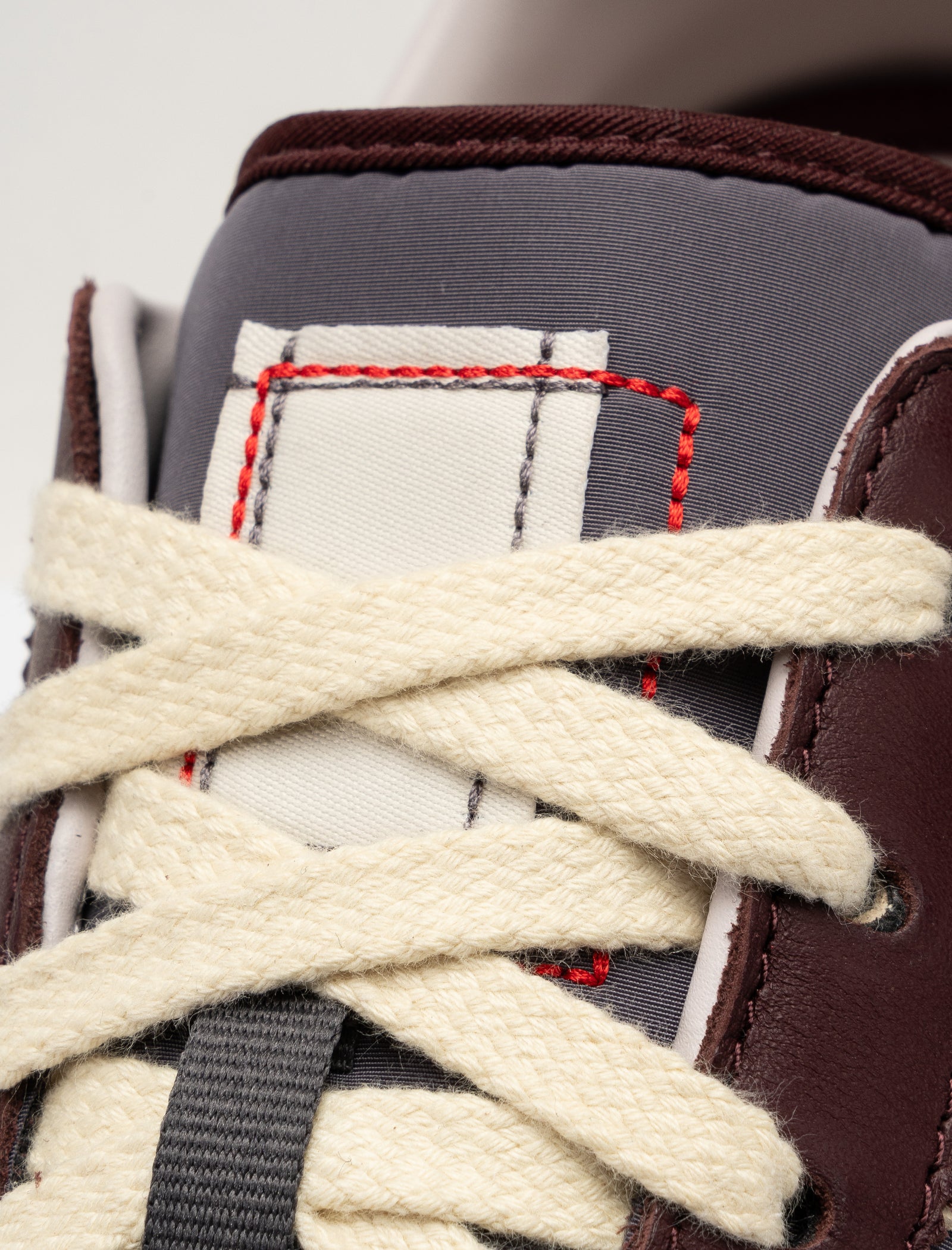 Close-up of the DND BW RUN HARLEM'S BEST low top sneaker with cream laces, gray tongue, and maroon upper. The tongue displays a white label outlined in red stitching.