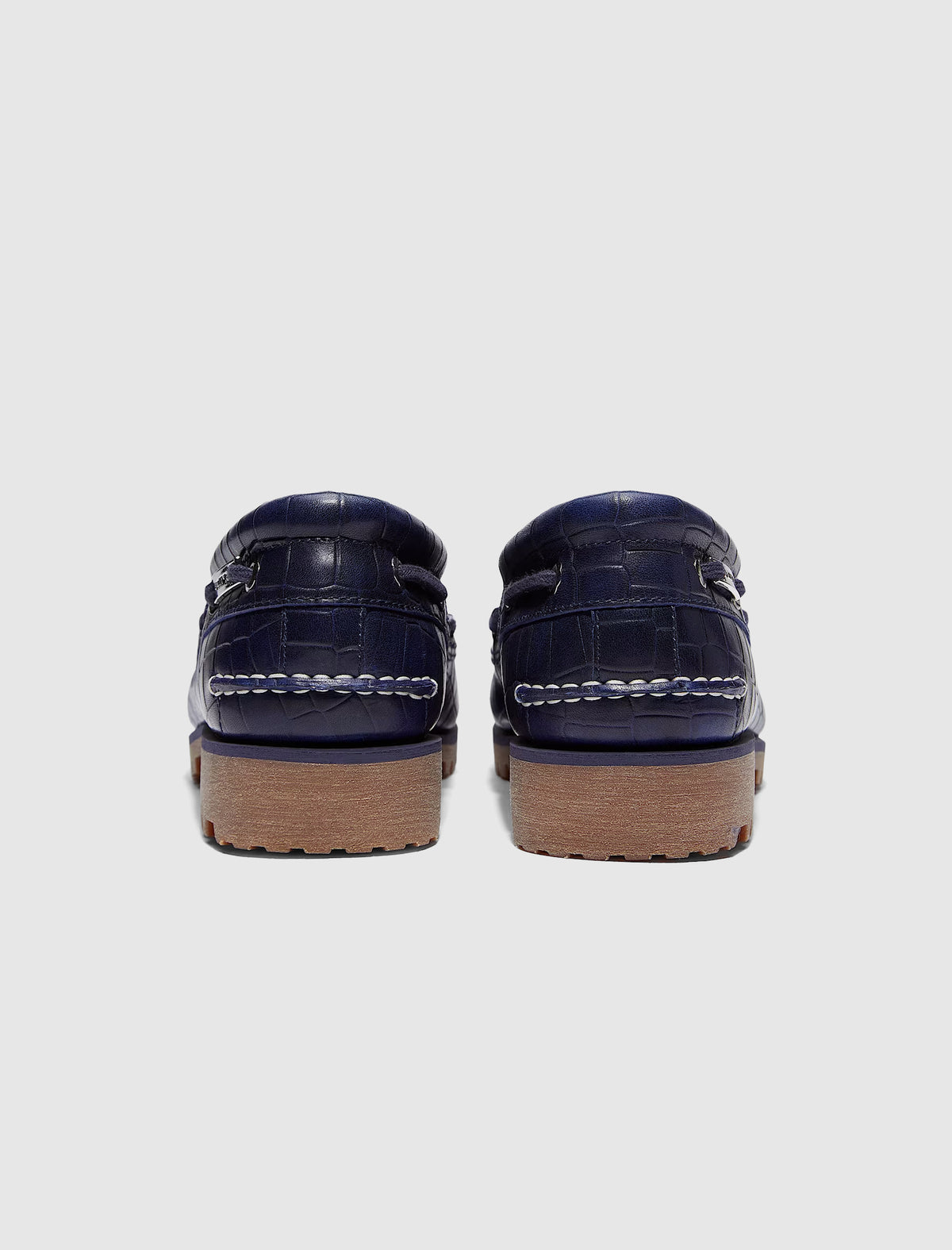 Rear view of navy blue crocodile-embossed leather TIMBERLAND X JACQUEMUS 3 EYE BOAT SHOE with thick, textured rubber soles.