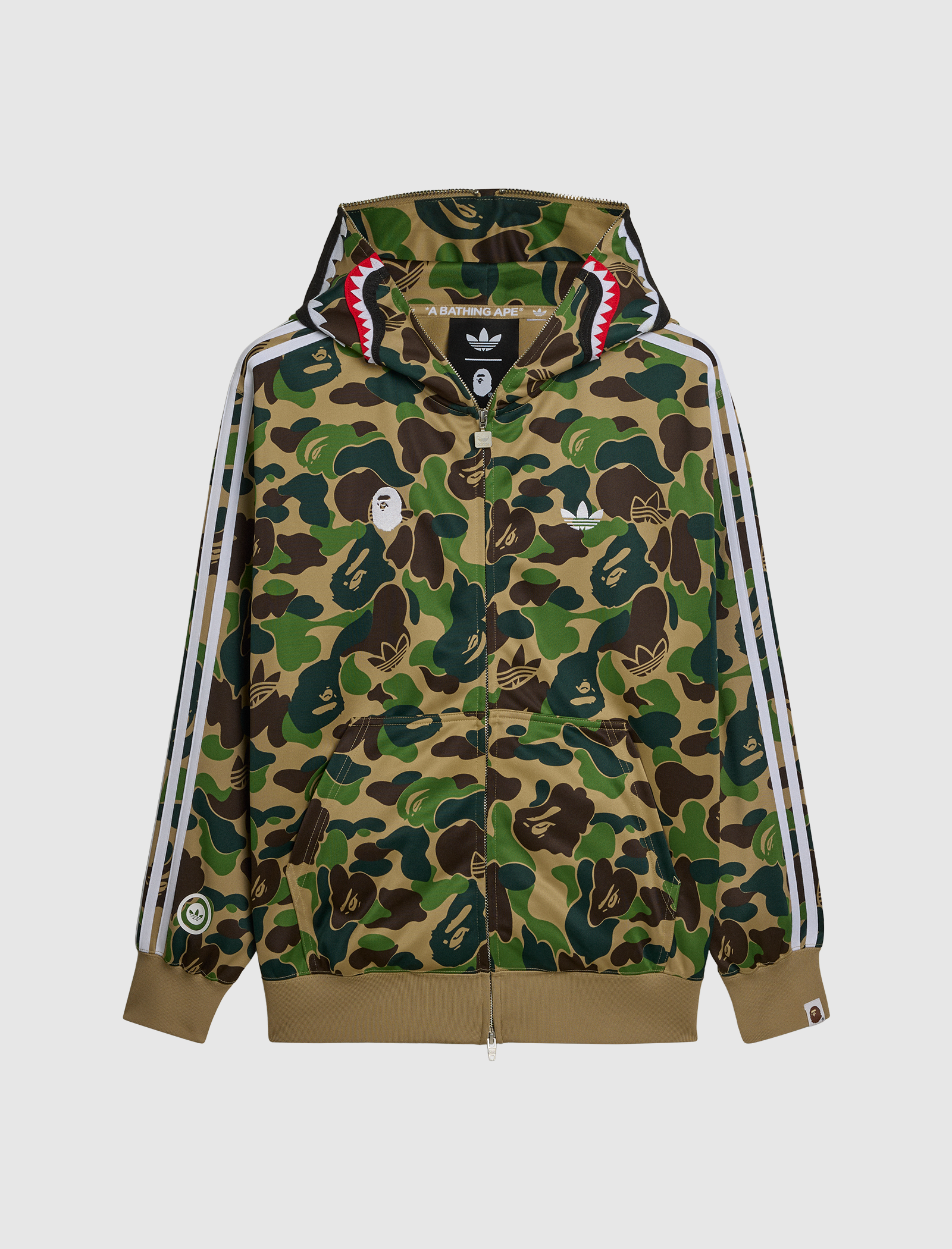 The SHARK TRACK HOODIE is a camo graphic hoodie in green, brown, and tan with white Adidas stripes, a shark mouth hood, and front Adidas x BAPE logos for a standout look.