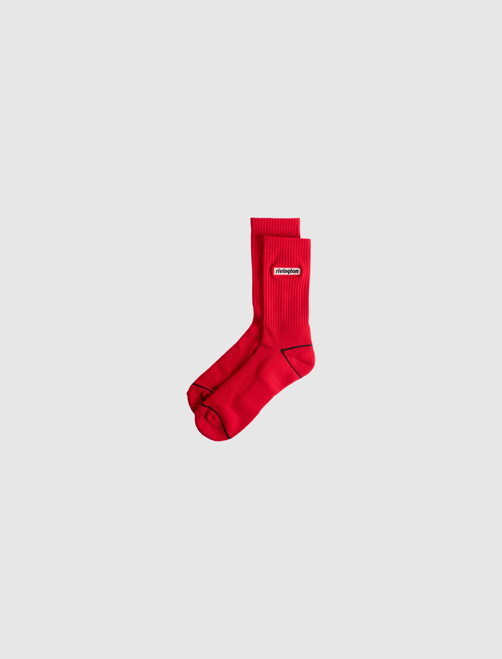 RIVINGTON SOCKS: Bright red crew-length socks with a ribbed texture and a rectangular white and red logo label on the side, shown against a plain light gray background.